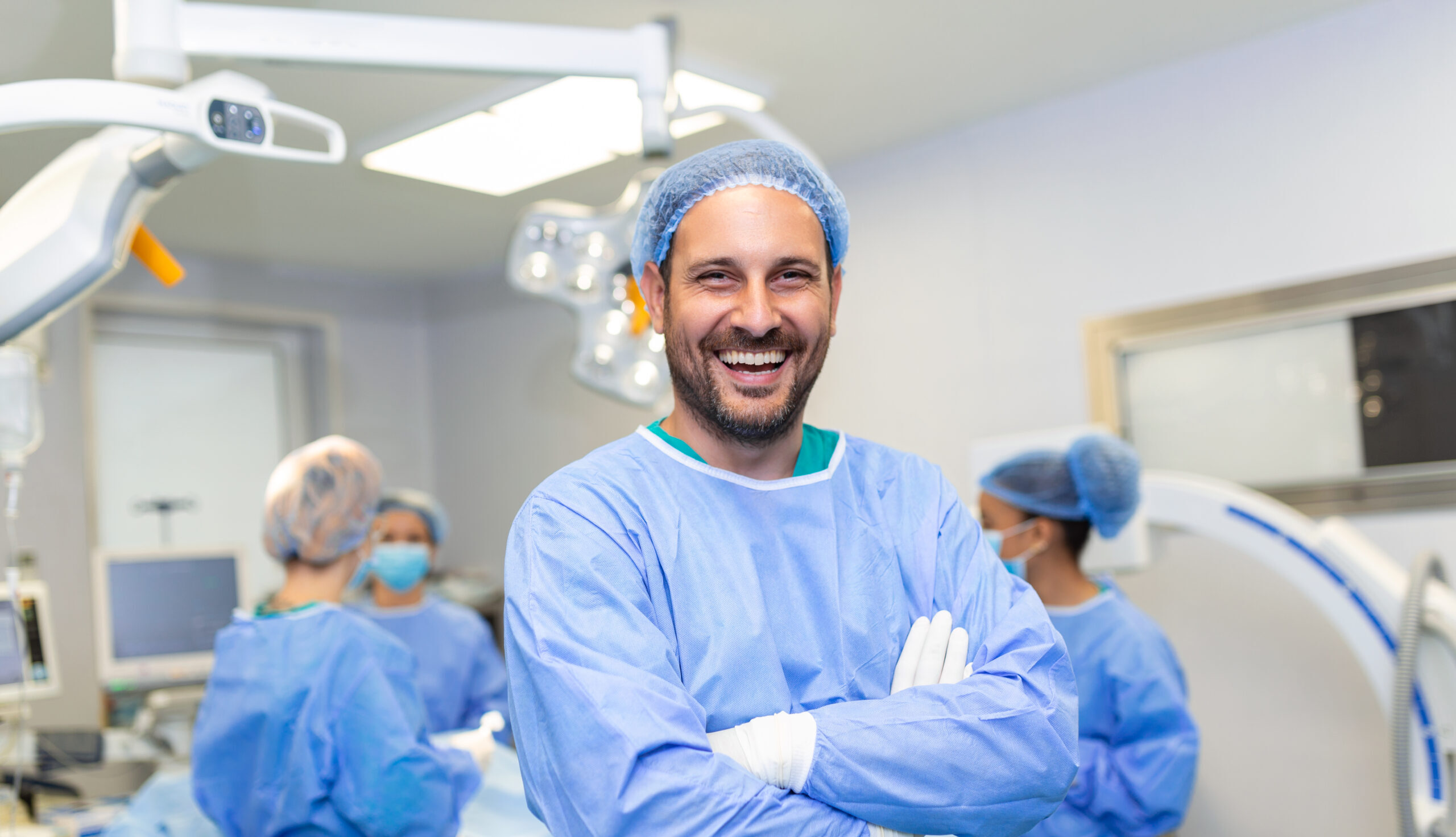 Portrait of male surgeon in operation theater looking at camera. Doctor in scrubs and medical mask in modern hospital operating room.
