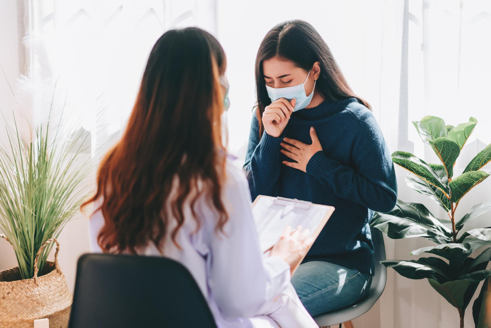 Patient wearing a mask coughing and holding her chest during a consultation about persistent cough and heart failure