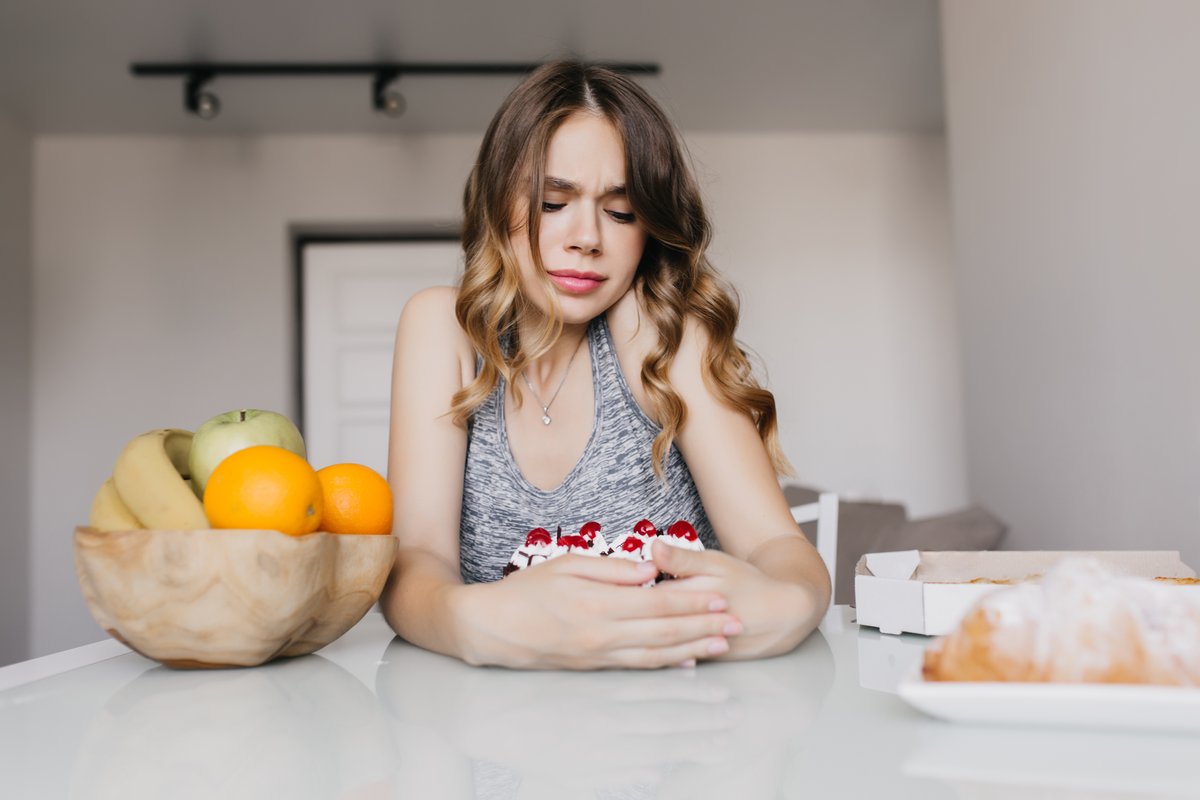 Woman at a kitchen table looking down at her plate with her hands clasped at her stomach, feeling full after small meals